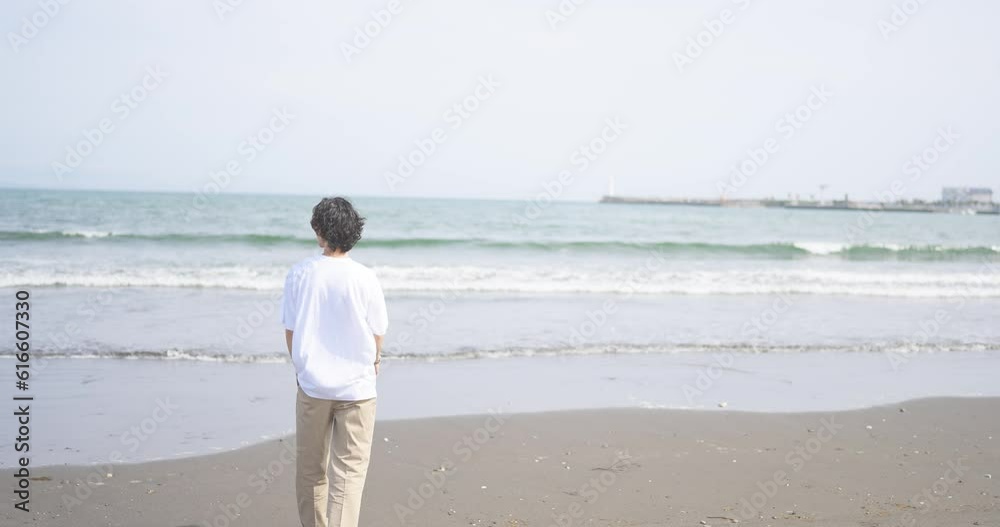 夏の海岸に向かって立つTシャツ姿の男性