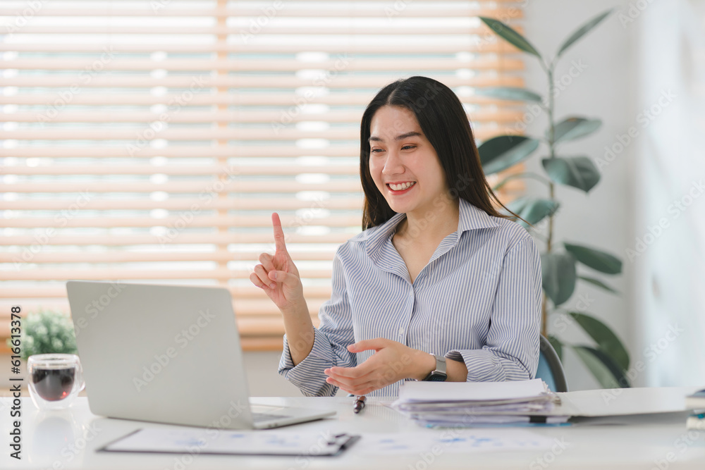 A cheerful businesswoman in casual is having a web conference at her kitchen table while working remotely from home. A cheerful businesswoman in casual is having a web conference at her kitchen table while working remotely from home.