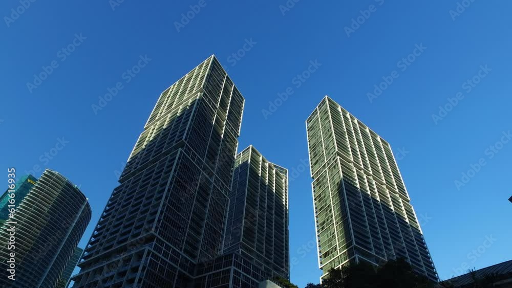 Aerial: Low Angle Panning Shot Of Modern Skyscrapers In City Against Blue Sky - Miami, Florida Aerial: Low Angle Panning Shot Of Modern Skyscrapers In City Against Blue Sky - Miami, Florida