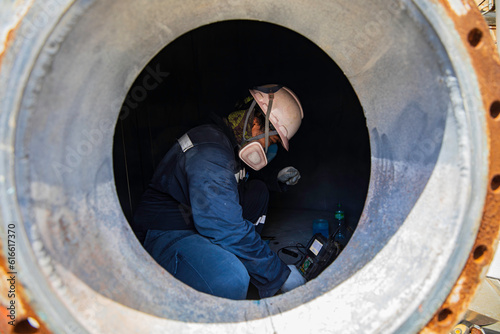 Male worker inspection scan tank of rust thickness bottom plate into confined photo