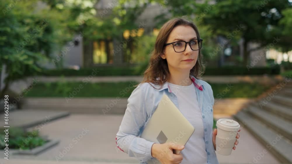 Woman walking on street with laptop and coffee in hands after work day Woman walking on street with laptop and coffee in hands after work day