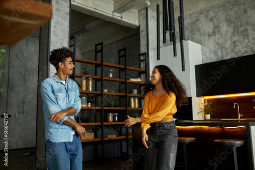 Indoor portrait of happy joyful smiling african american male and female in stylish loft style kitchen, looking at each other and flirting while dancing and gesticulating, girl having fun