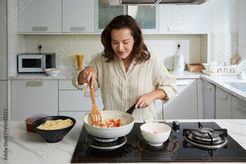 Photo Smiling woman enjoying smell of frying vegetables when cooking spaghetti sauce f