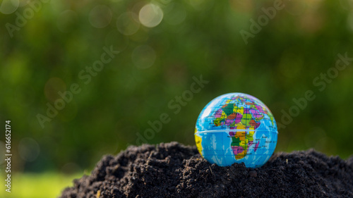 The small globe, earth is on hand, grass, leaf. The globe has maps on it and environmental map. The earth map shown geography continents, countries. The globe ball is the symbol of our planet earth.