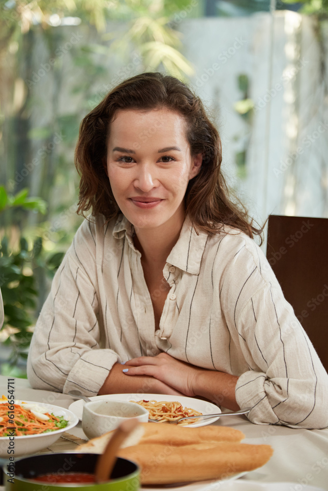 Portrait of smiling woman in striped shirt sitting at dinner table at home