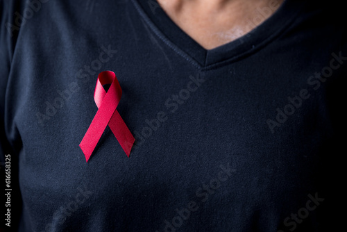 The red ribbon stick on black T-shirt. A person has a ribbon hang on shirt. The ribbon is the symbol of prevention HIV day. The awareness training opening ceremony day have a lots of red ribbons.