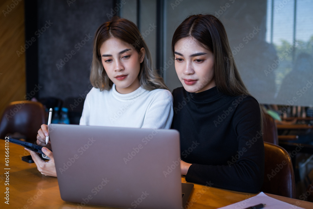 Two cheerful young Asian female college students working on the school project using laptop computers and tablets together in private study room Two cheerful young Asian female college students working on the school project using laptop computers and tablets together in private study room