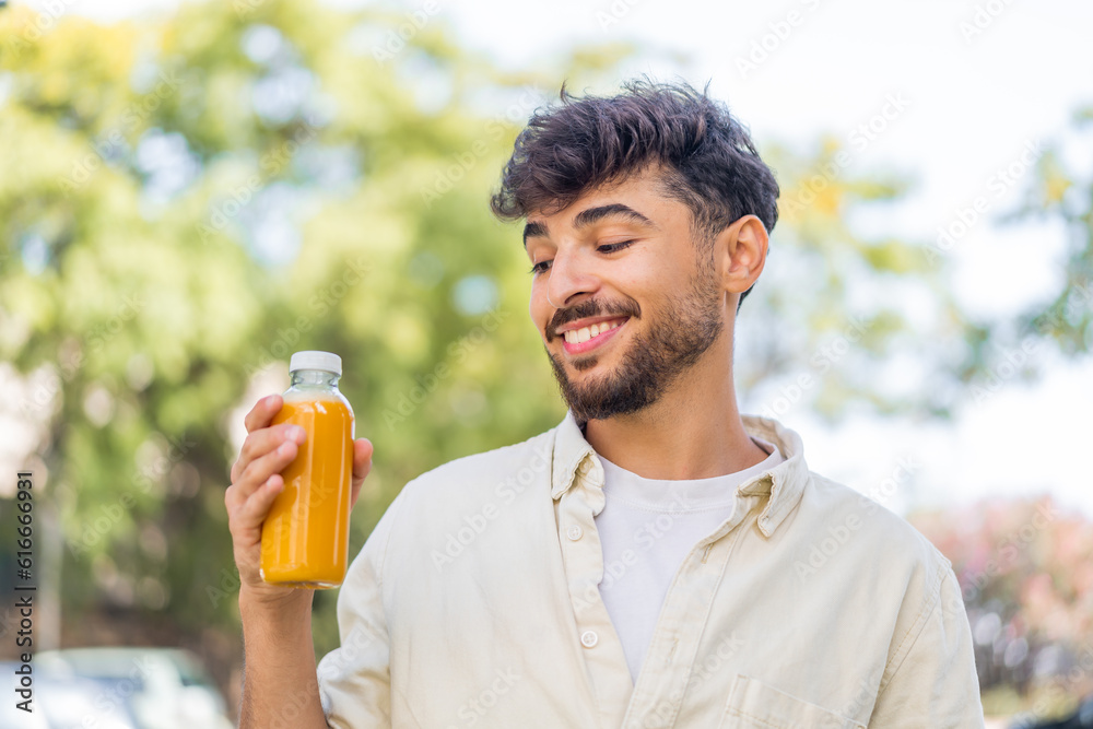 Fototapeta premium Young Arabian handsome man holding an orange juice at outdoors with happy expression