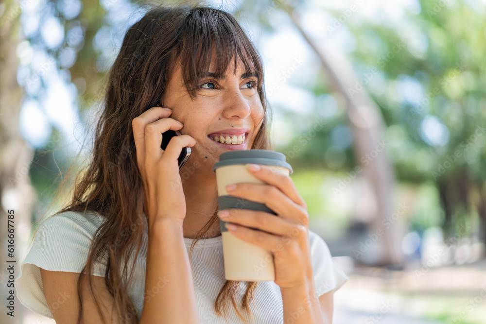 Young woman at outdoors using mobile phone and holding a coffee with happy expression Young woman at outdoors using mobile phone and holding a coffee with happy expression