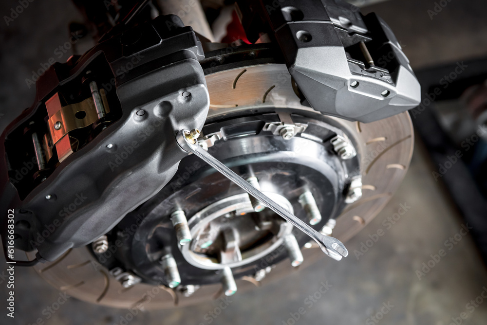 Car mechanic or serviceman disassembly and checking a disc brake and asbestos brake pads for fix and repair problem at car garage or repair shop Car mechanic or serviceman disassembly and checking a disc brake and asbestos brake pads for fix and repair problem at car garage or repair shop
