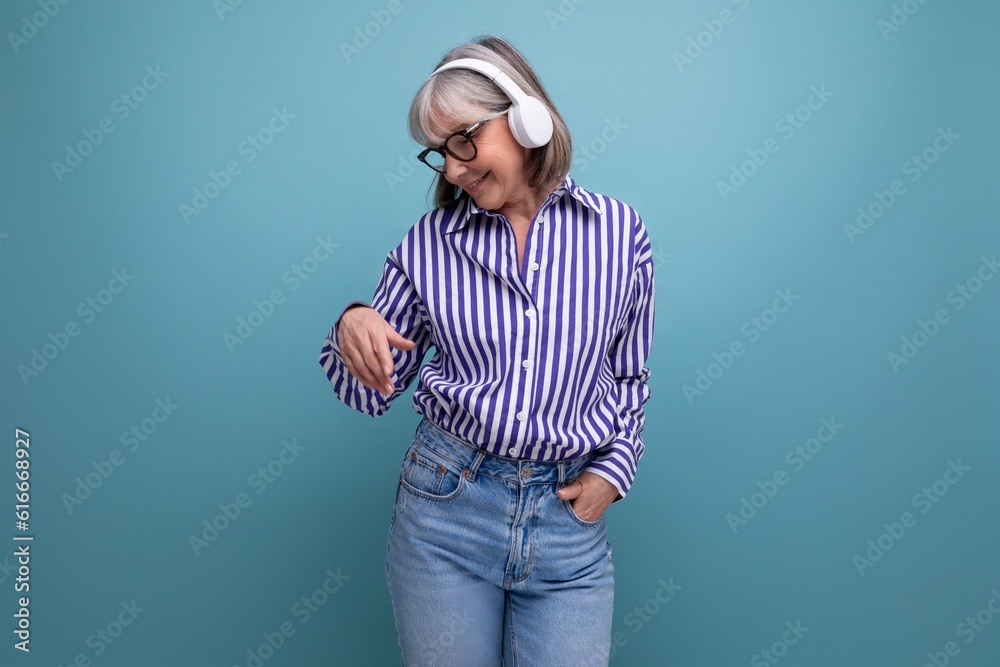 energetic retired woman with gray hair getting acquainted with gadgets for music on a bright studio background