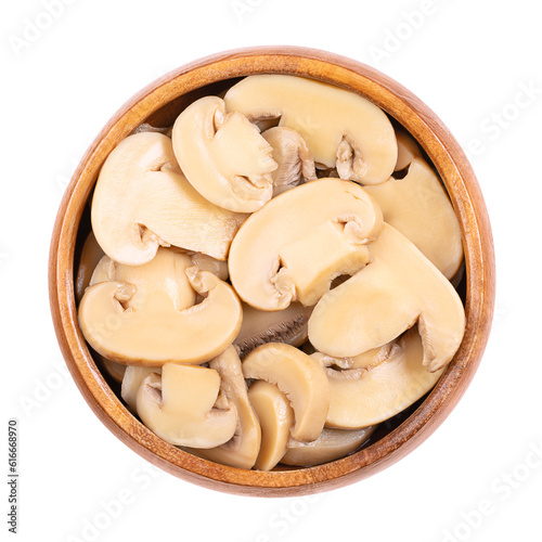 Canned sliced white champignon mushrooms, in a wooden bowl. Agaricus bisporus, also called common, button, cultivated or table mushroom. Close-up from above, isolated on white background, food photo.