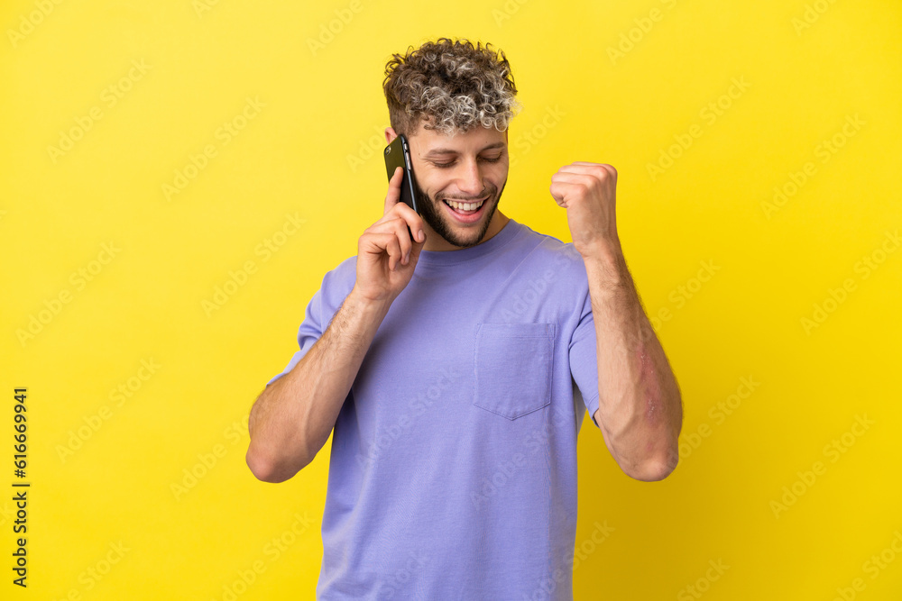 Young caucasian man using mobile phone isolated on yellow background celebrating a victory Young caucasian man using mobile phone isolated on yellow background celebrating a victory
