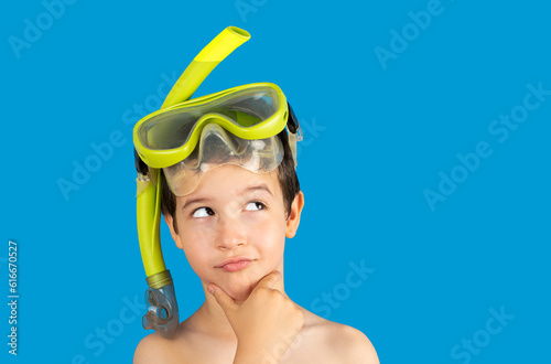 Child with mask tuba and snorkel with hand on chin thinking about question, thoughtful expression.Concept of doubt and looking aside. Snorkeling, swimming, vacation concept isolated on blue background
