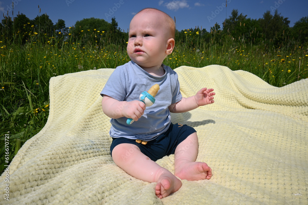 A 7monthold toddler sits on a blanket in the park and eats