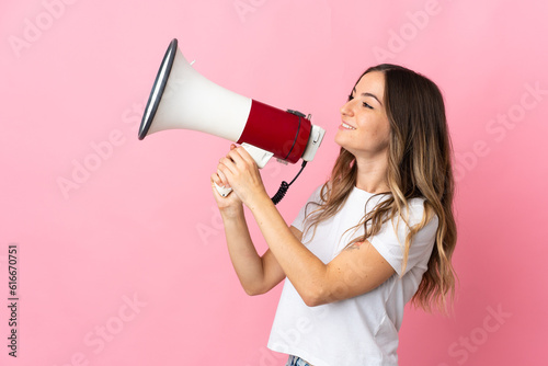 Young Romanian woman isolated on pink background shouting through a megaphone to announce something