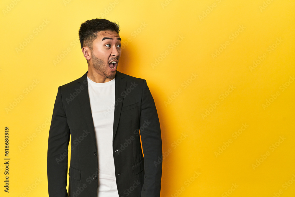 Asian man in black business jacket on yellow studio being shocked because of something she has seen. Asian man in black business jacket on yellow studio being shocked because of something she has seen.