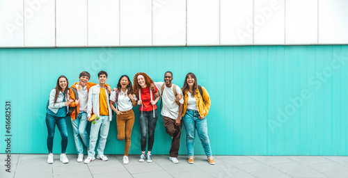 Diverse college students standing together on a blue wall - Photo portrait of multiracial teenagers in front of university building - Life style concept with guys and girls going to highschool photo