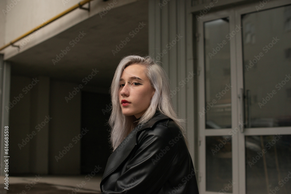 Portrait of a young beautiful girl in a black coat walking around the city. Subculture