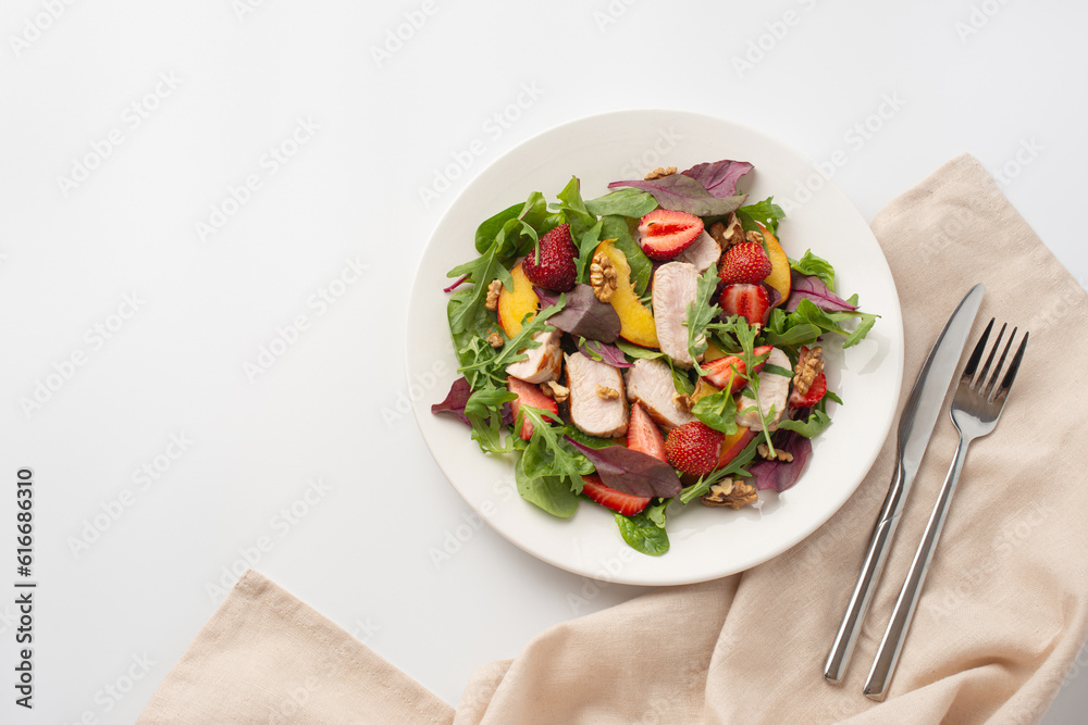 Salad with chicken, mango, strawberries and green leaves on a white background