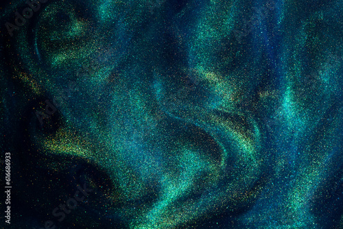 Various stains and overflows of gold particles in blue fluid with green tints. Golden particles dust and smooth defocused background. Liquid iridescent shiny backdrop with depth of field.