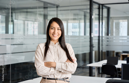 Confident smiling young professional Asian business woman corporate leader, happy japanese female employee, company sales marketing manager, standing arms crossed in office, portrait.