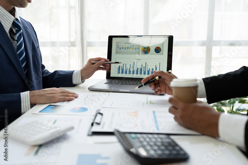 Financial analyst analyzing business financial report on laptop and graph document during discussion in company showing successful teamwork business meeting concept marketing.