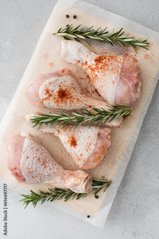 Raw chicken legs with spices and rosemary sprigs on a wooden cutting board. Raw chicken legs with spices and rosemary sprigs on a wooden cutting board.