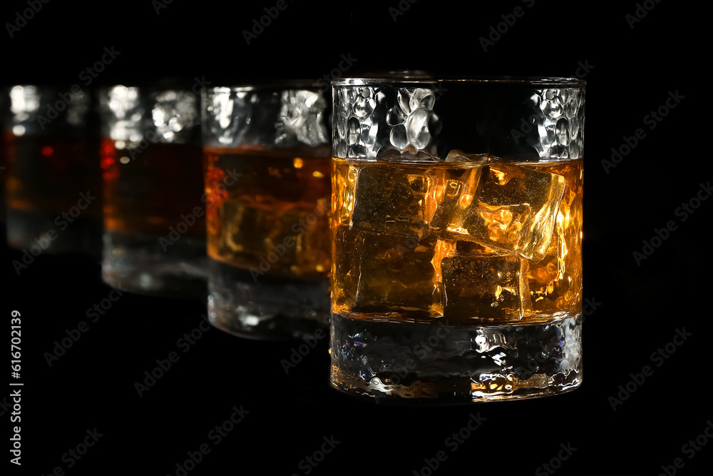 Four glasses of bourbon whiskey are illuminated by fire, and stand in one line towards the frame, on a black background Four glasses of bourbon whiskey are illuminated by fire, and stand in one line towards the frame, on a black background
