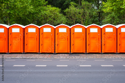 A line of orange plastic portable chemical toilets photo