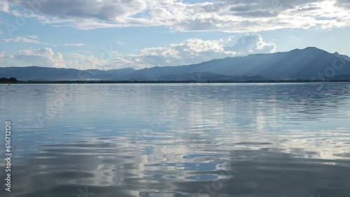 Water surface of Phayao Lake is moving smoothly and calmly looking relaxed with the horizon, clouds and mountains in the background
