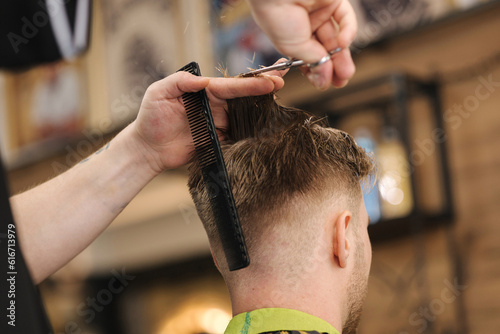 Back view of barber using scissors and making hairstyle. Modern barbershop