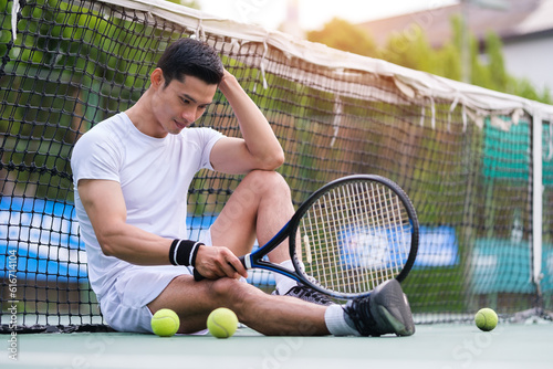 Exhausted man tennis player sitting on the court looking disappointed after practice. © wattana