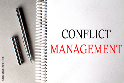 CONFLICT MANAGEMENT text on a notebook with pen on grey background