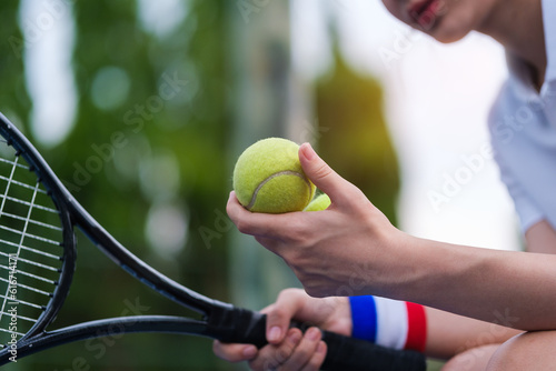 Closeup of female hand holding tennis ball and racket while playing tennis on a sunny day. © wattana