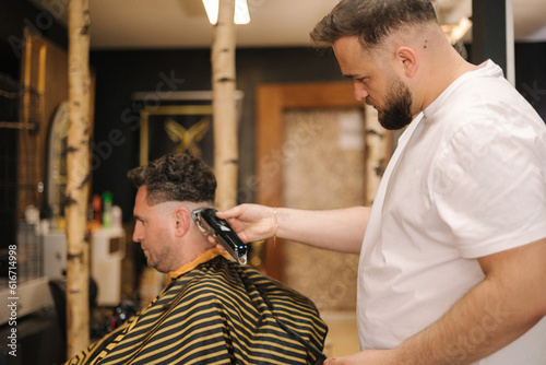 Professional hairdresser cuts hair of confident man in barbershop