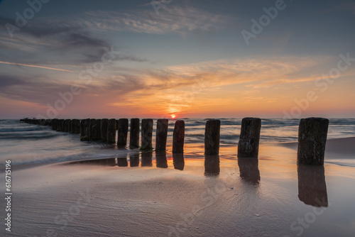 Sunset on Baltic sea shore with old wooden breakwater poles sticking out of the sea in Bernati, Latvia. Long exposure photography. photo