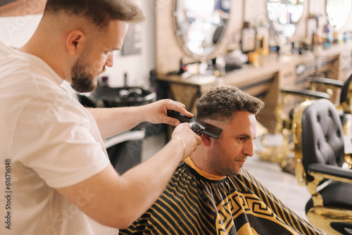 Professional hairdresser cuts hair of confident man in barbershop