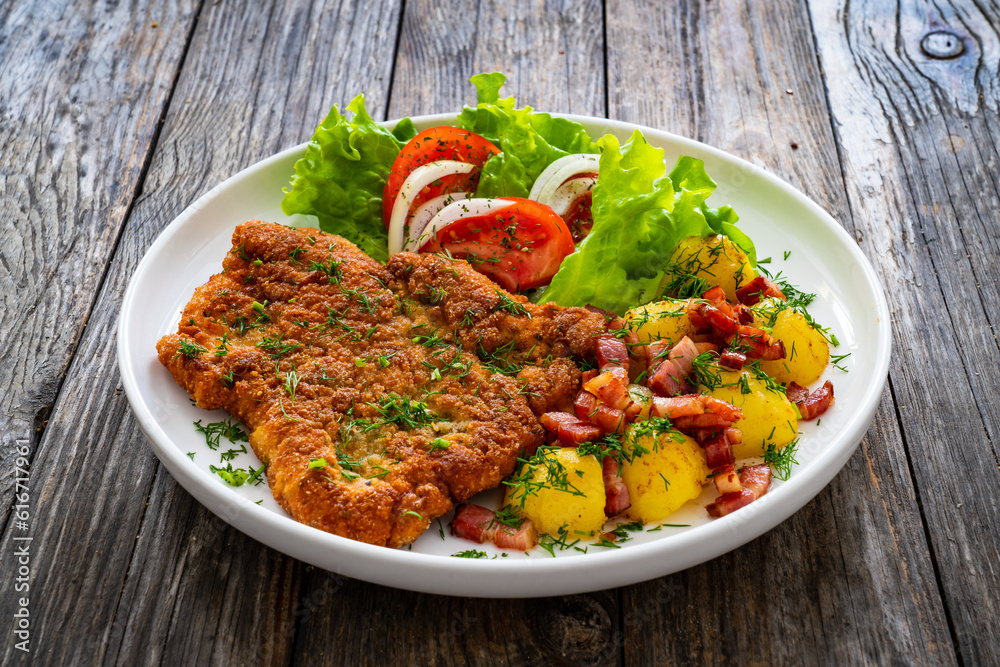 Breaded fried pork chop with fresh vegetable salad and potatoes on wooden table
Breaded fried pork chop with fresh vegetable salad and potatoes on wooden table