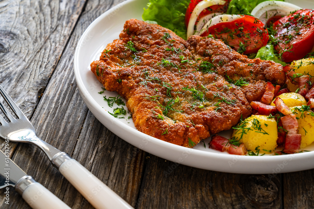 Fototapeta premium Breaded fried pork chop with fresh vegetable salad and potatoes on wooden table 