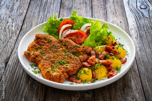 Breaded fried pork chop with fresh vegetable salad and potatoes on wooden table
