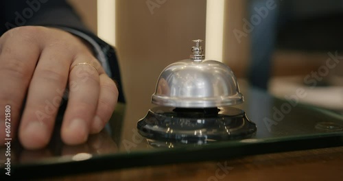 Close-up of businessman's hand rigning bell at hotel reception desk while client is arriving and waiting for check-in. Accommodation and tourism concept. photo