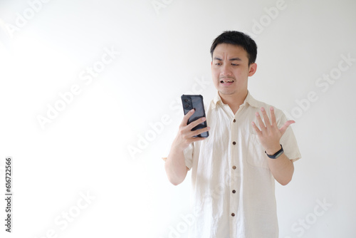 A young Asian man wearing a beige shirt and a smartwatch on his left wrist is in conversation via video call on a smartphone. Isolated white background. Suitable for advertisement.