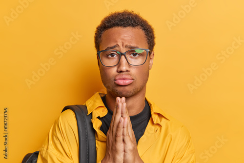 Photography Displeased African man keeps palms together has pity expression wears spectacles