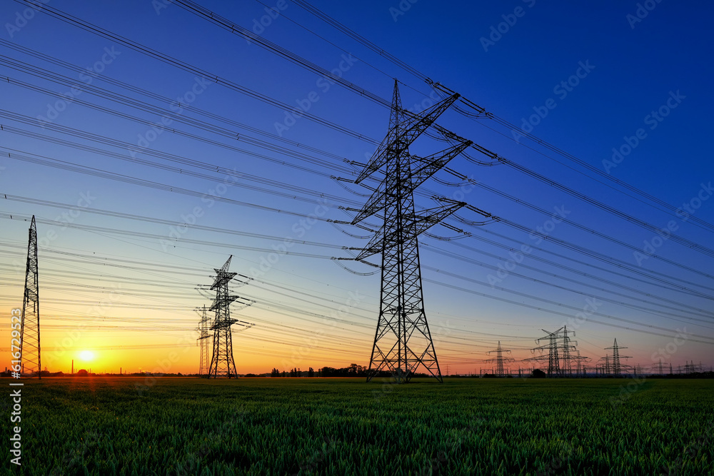 Sunrise with blue morning sky over the fields with high voltage energy tower. Landscape with high tension electrical energy mast.