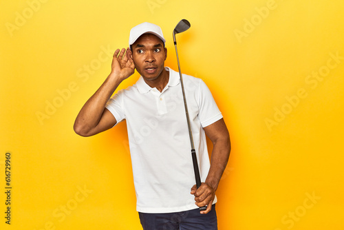 African American man golfer  yellow studio backdrop  trying to listening a gossip.