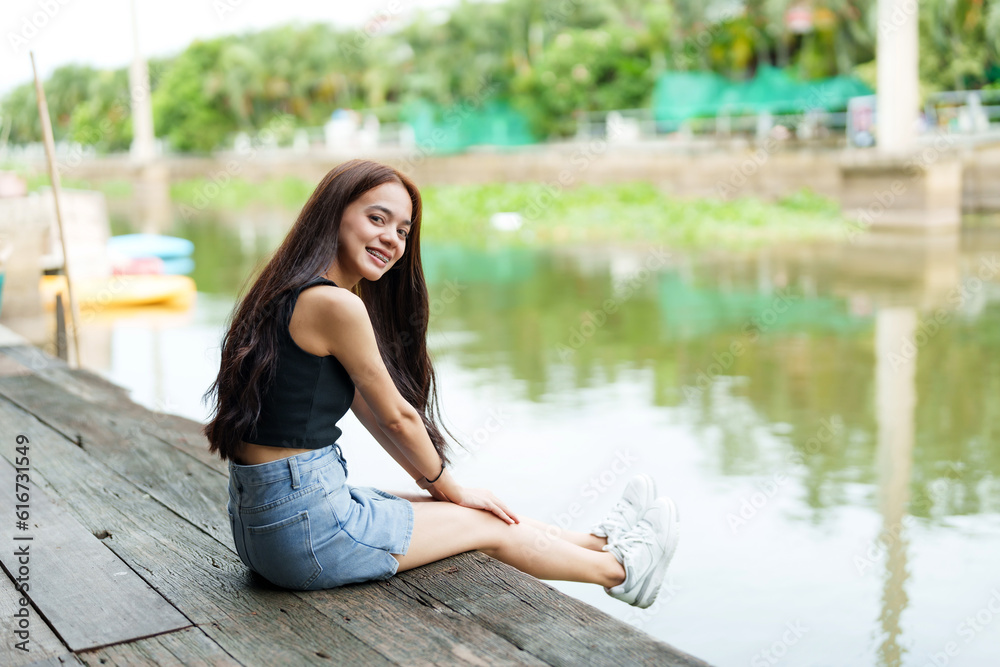 Cute Asian girl with long hair sitting and relaxing in her free time on the pier By the river on weekends with smiling faces A rural canal with clear water