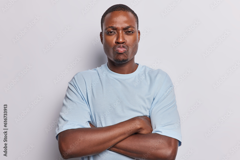Grumpy offended dark skinned man keeps arms folded feels insulted after quarrel doesnt want to speak with you dressed in casual t shirt isolated over white background. Negative human emotions Grumpy offended dark skinned man keeps arms folded feels insulted after quarrel doesnt want to speak with you dressed in casual t shirt isolated over white background. Negative human emotions