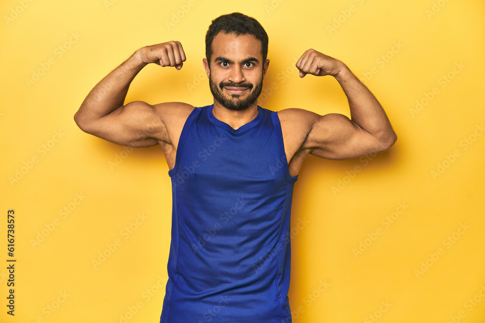Muscular Latino man in sportswear flexing muscles, yellow studio background. Muscular Latino man in sportswear flexing muscles, yellow studio background.