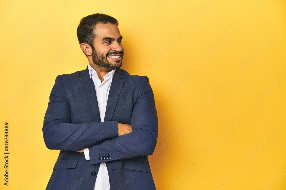 Professional young Latino man in business suit, yellow studio background, smiling confident with crossed arms. Professional young Latino man in business suit, yellow studio background, smiling confident with crossed arms.